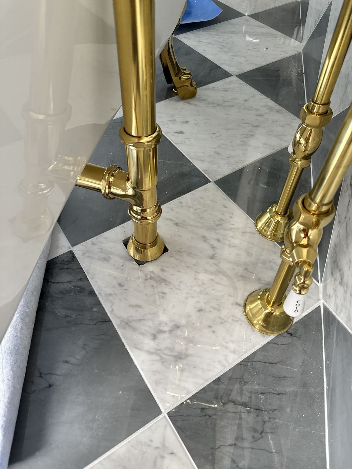 Brass tub filler and supply lines installed on a checkered tile floor by Precision Plumbing Solutions