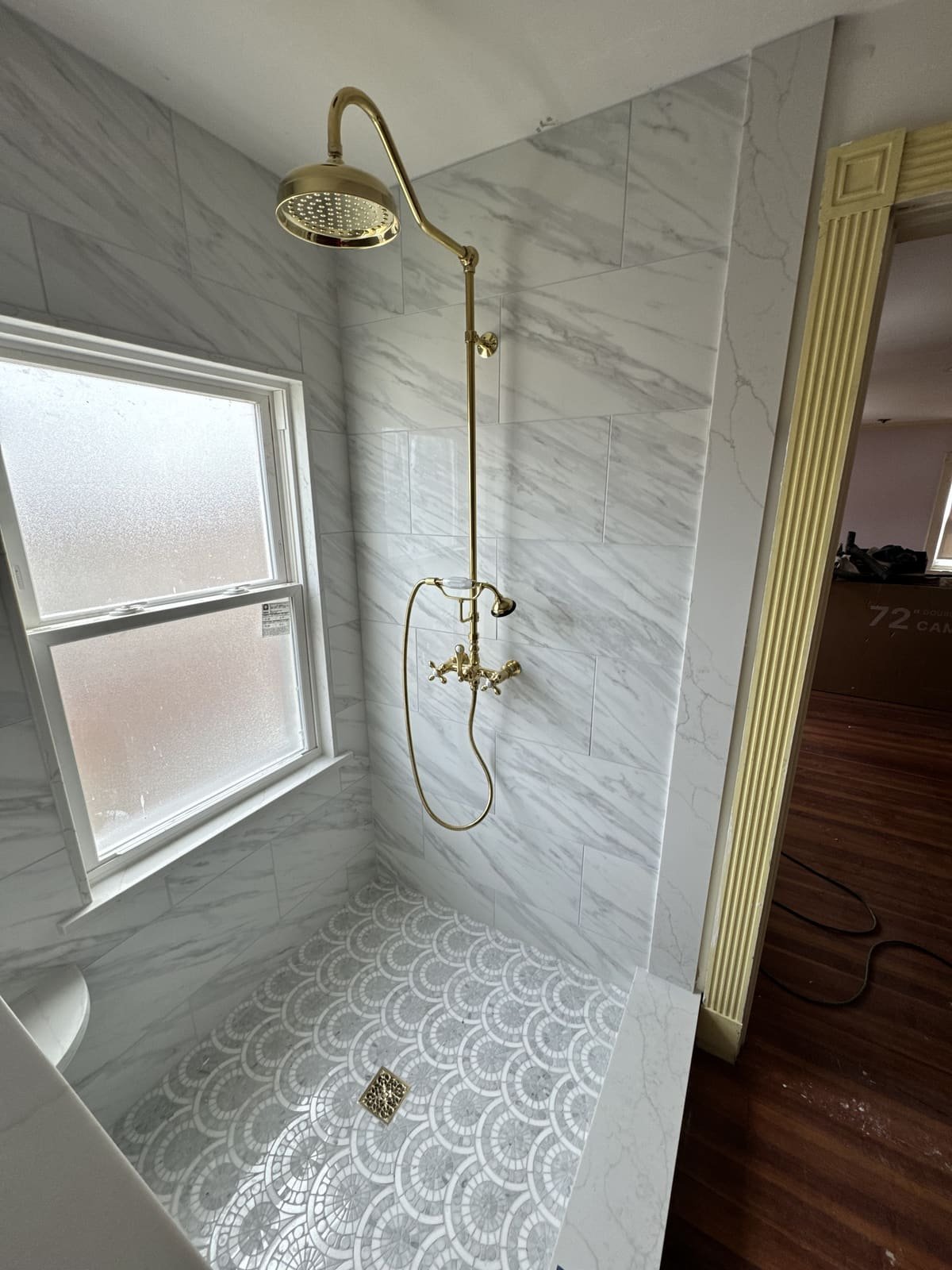 Marble walk-in shower with brass rain head and hand shower installed by Precision Plumbing Solutions